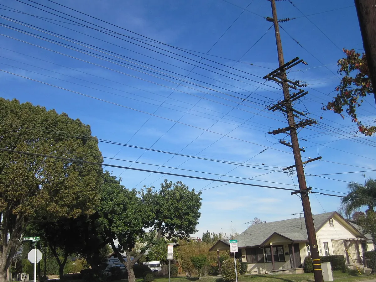 A corner in Monterey Park with mature trees, a utility pole and a small house with a gabled roof